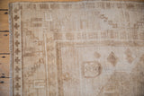 Corner of distressed Oushak carpet, showing geometric border, fringe, and worn sand beige pile.