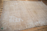 Distressed Oushak corner with geometric borders, sand, pale coffee, and even textured wear.