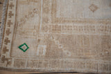 Detail of distressed Oushak rug with emerald green motif and worn sand-tone pile.