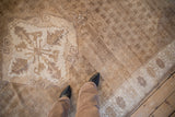 Distressed Oushak rug's serrated medallion and floral elements in pale coffee brown, cream hues.