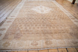 Distressed Oushak rug corner showing repeating floral trellis, patterned border, and fringe.