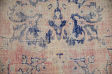 Close-up of distressed Oushak rug with soft pink, cobalt blue motifs, and visible worn pile.