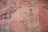 Detail of distressed Oushak rug's pink abrashed field, curvilinear spandrel, and vine-seed motif border.