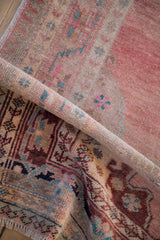 Folded vintage Oushak rug showcasing distressed pile, vine and pawn border motifs in blush, teal, aubergine.