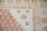 Distressed Oushak rug corner, dusty copper stepped border with ivory abrash lattice.