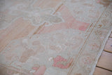 Angled view of the distressed, low-pile texture on a vintage Oushak rug in dusty rose and silver.