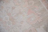 Low-pile, hand-knotted texture of a distressed Oushak in sand and pale blush tones.