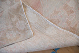 A folded corner reveals the hand-knotted construction and soft pile of a vintage Oushak rug.
