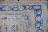 Distressed vintage Oushak rug corner, cobalt blue border, soft ivory and pale blue floral field.
