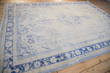Distressed Oushak rug corner showing worn cobalt blue floral borders and faded ivory field.