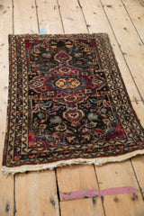 Angled view of a vintage Lilihan rug showing its charcoal floral field and textured, time-worn character.