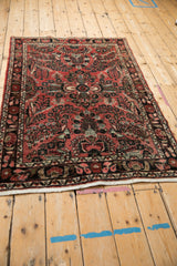 Vintage Persian rug corner: faded raspberry field, dark navy floral border, white fringe.