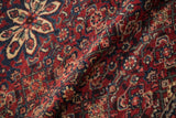 Folded vintage Hamadan rug pile revealing intricate Herati patterns in cherry red, cobalt blue, and ivory.