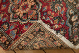 Corner of vintage Lilihan rug, showing hand knotted foundation, red palmettes, and white fringe.