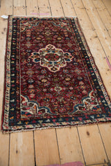 A vintage Hamadan rug from an angle, showcasing its burgundy field and scalloped center medallion.