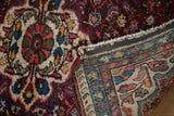 A folded corner of the vintage Hamadan rug shows its hand-knotted foundation and thick floral pile.