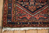 Vintage Hamadan rug corner, displaying madder root red border, meandering vine patterns, and white fringe.