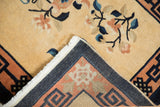 Peking rug folded corner showing beige floral pile, dark geometric border reverse, blue-tinged fringe.
