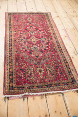 Angled view of a vintage Sarouk rug highlighting its raspberry red field and meandering floral vine border.