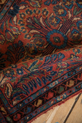 Folded vintage Mehriban rug pile reveals brick red, sapphire blue, and green floral vine motifs.