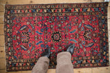 Textured pile of antique Lilihan rug, displaying raspberry red field with blue blossoms and scrolling vines underfoot.
