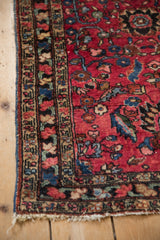 Corner of antique Persian Lilihan rug with rich raspberry red field, scrolling floral motifs, and patterned border.