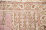 Distressed texture and pale pink, brown pinwheel floral motifs on a vintage Mazlaghan rug.
