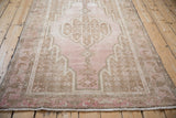 Fringed corner of vintage Mazlaghan rug, featuring geometric border in aged pink and brown.