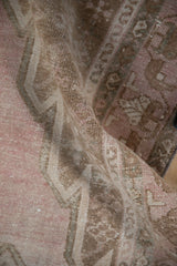 Folded vintage Mazlaghan rug with muted pink, coffee brown pile, wear revealing foundation.