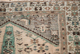 Corner detail of a distressed vintage Hamadan rug, showing faded beige and emerald green motifs.