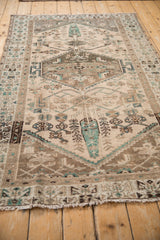 Distressed Hamadan rug showing faded emerald green motifs on a worn beige field with fringe.