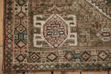 Geometric patterns and fringe of a vintage Qashqai rug in dusty mauve, emerald green, and camel tones.