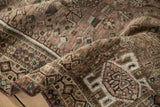 Folded vintage Qashqai rug with geometric patterns in dusty mauve, beige, and emerald green.
