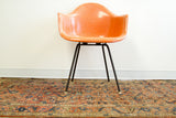 Shabby antique Persian rug featuring tribal Herati design in faded pinkish red, under chair.