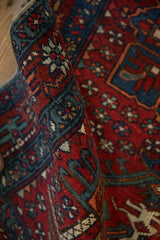 Rolled Karaja rug showing fine weaving with cherry red pinwheel blossoms and dusty teal border.