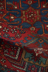 Rolled pile of a vintage Karaja rug, showing cherry red pinwheel florals and sapphire blue vine patterns.
