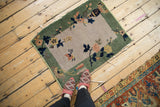 Antique Nichols Art Deco rug mat with ivory field, celadon border, floral design, tattered edges.