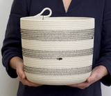 Woven rope basket with black zigzag stitching held to demonstrate scale.