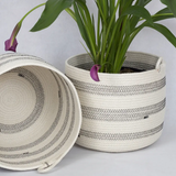 Cylindrical woven rope basket in a natural cream color with bands of black zigzag stitching.