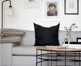 Black linen pillow with exposed brass zipper and leather pull on a gray sofa.