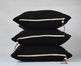 Stacked black 27x27 linen pillows with brass zippers and leather pulls, wood beads.