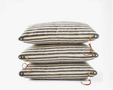Stacked heavy linen lumbar pillows, dark gray and off-white stripes, brass zippers, leather pulls.