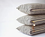 Stacked charcoal and natural linen striped lumbar pillows, brass zippers, leather pull.