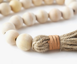 A genuine leather wrap secures a textured jute tassel on a garland of wood beads.