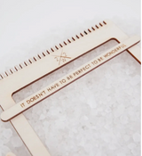 Light wood weaving loom component with engraved inspirational message and notches.