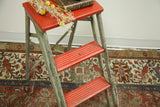 Distressed red wooden steps and worn silver frame of the vintage industrial step stool.
