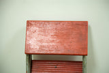 Distressed red wooden top of industrial step stool with chips, crack, and aged patina.