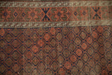 Antique Belouch rug close-up: geometric diamond pattern in faded raspberry, navy, brown, low pile.