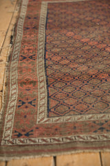 Antique Belouch rug corner with faded raspberry, navy geometric patterns, tattered side selvage, visible foundation.