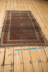 Antique Belouch rug corner showing geometric diamond pattern, significant pile wear, tattered fringe.